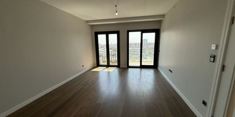 Boş bir dairenin ahşap parkeli odası; siyah çerçeveli iki balkon kapısından şehir görünüyor