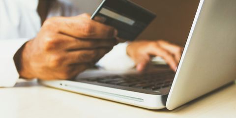 Bir elinde banka kartı, diğeriyle dizüstü bilgisayarda ödeme ekranını dolduran kişi