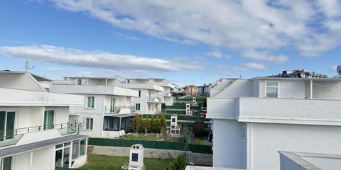 Rows of white detached houses with gardens on a hillside under a blue sky, seen from an upper floor