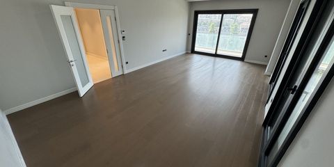 An empty room in a new apartment, dark wood flooring, a white double door to the hall and a sliding balcony door with the city beyond